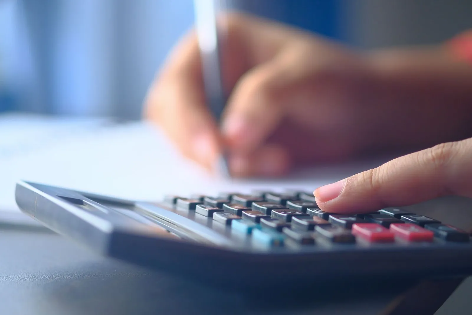 Hand using a calculator while writing budget figures on paper