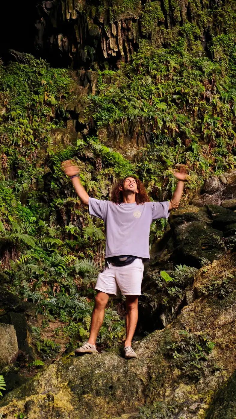 Traveler raising both arms in celebration inside a mossy Vietnamese cave