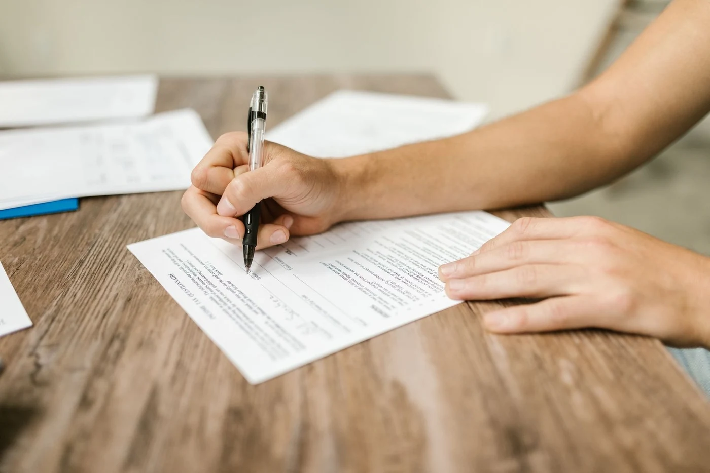 Hand filling in a paper form with a pen at a desk