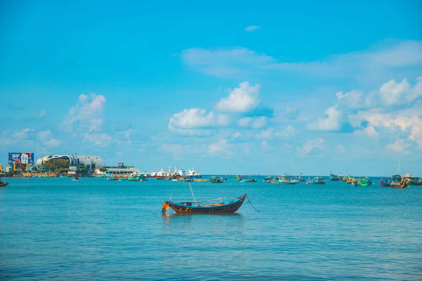 Fishing boats at anchor in a blue bay with the Vung Tau waterfront in the distance