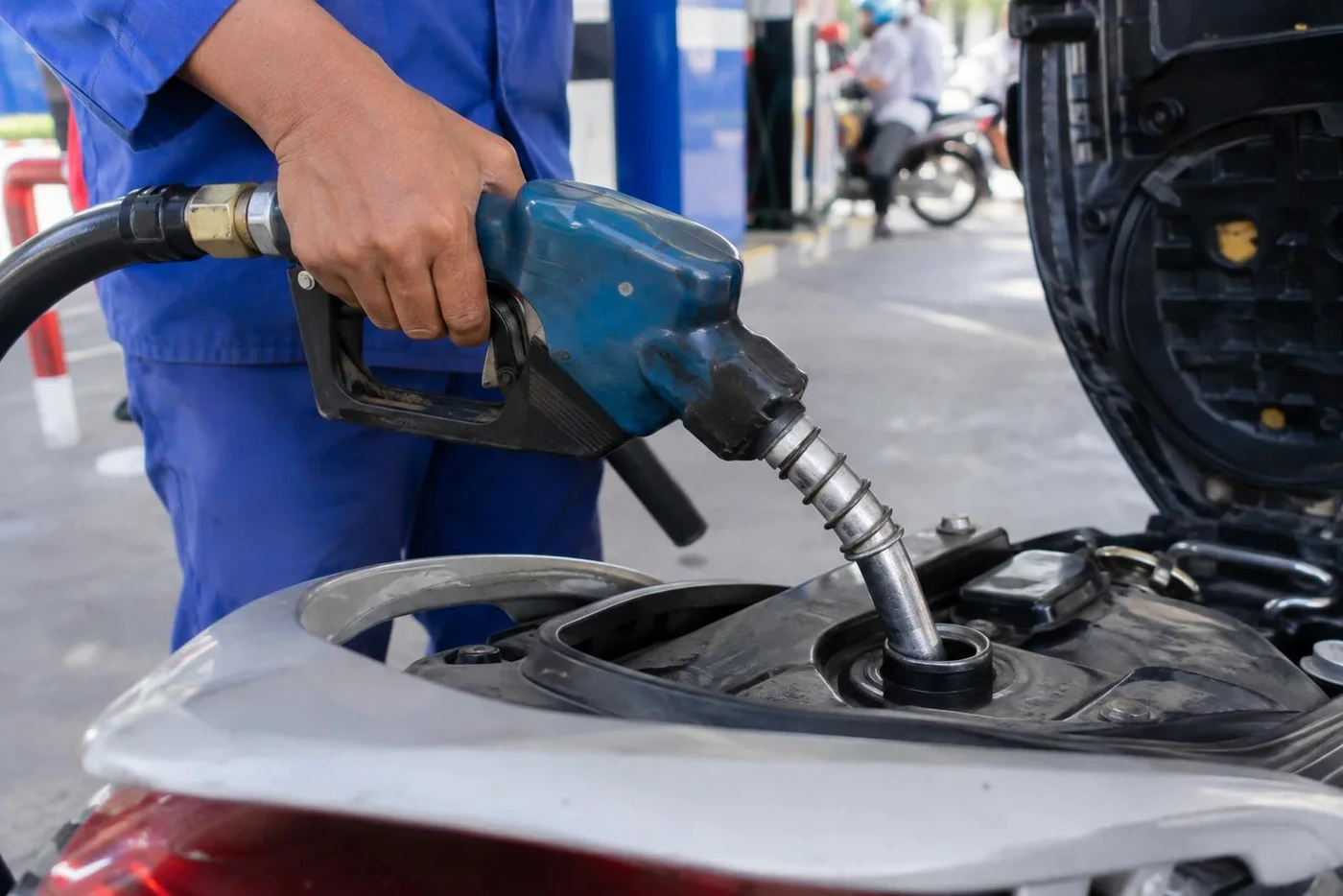 Attendant filling a scooter fuel tank at a petrol station