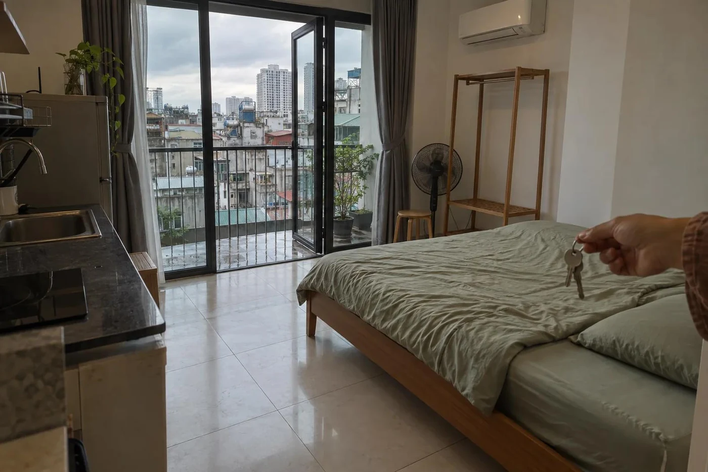 Hand holding apartment keys in a furnished studio with a balcony