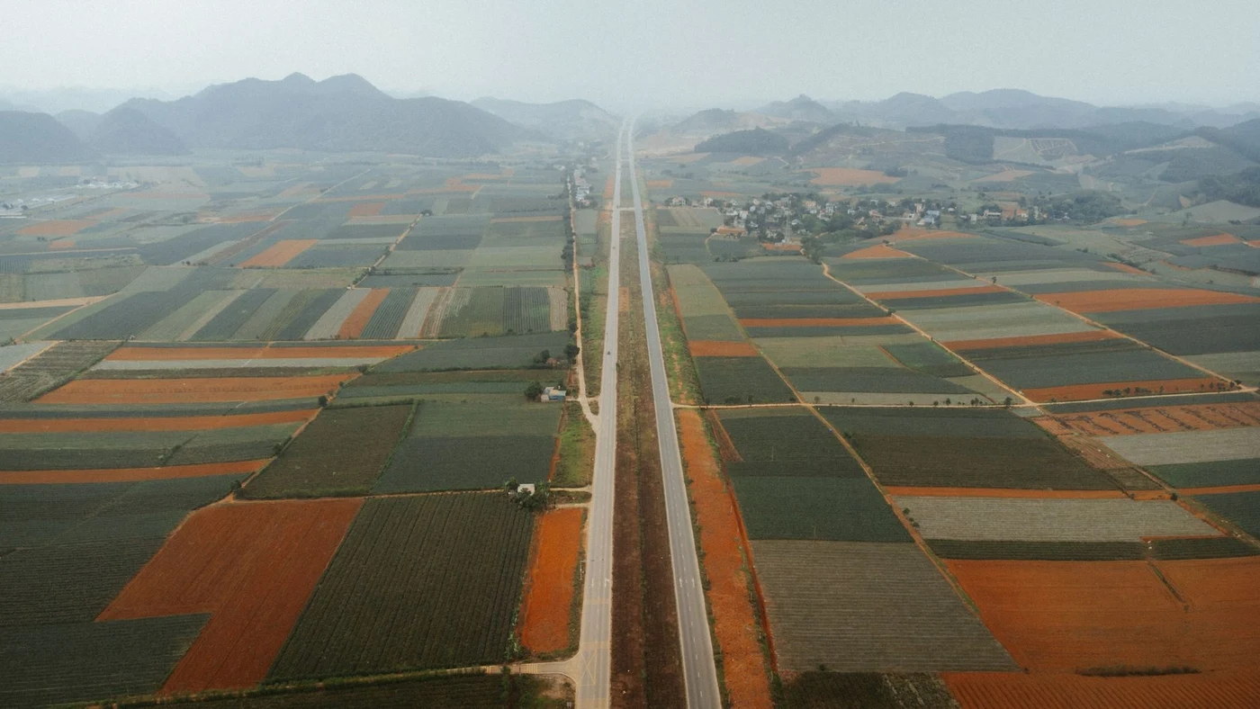 Aerial view of a two-lane highway running through farmland toward misty mountains.