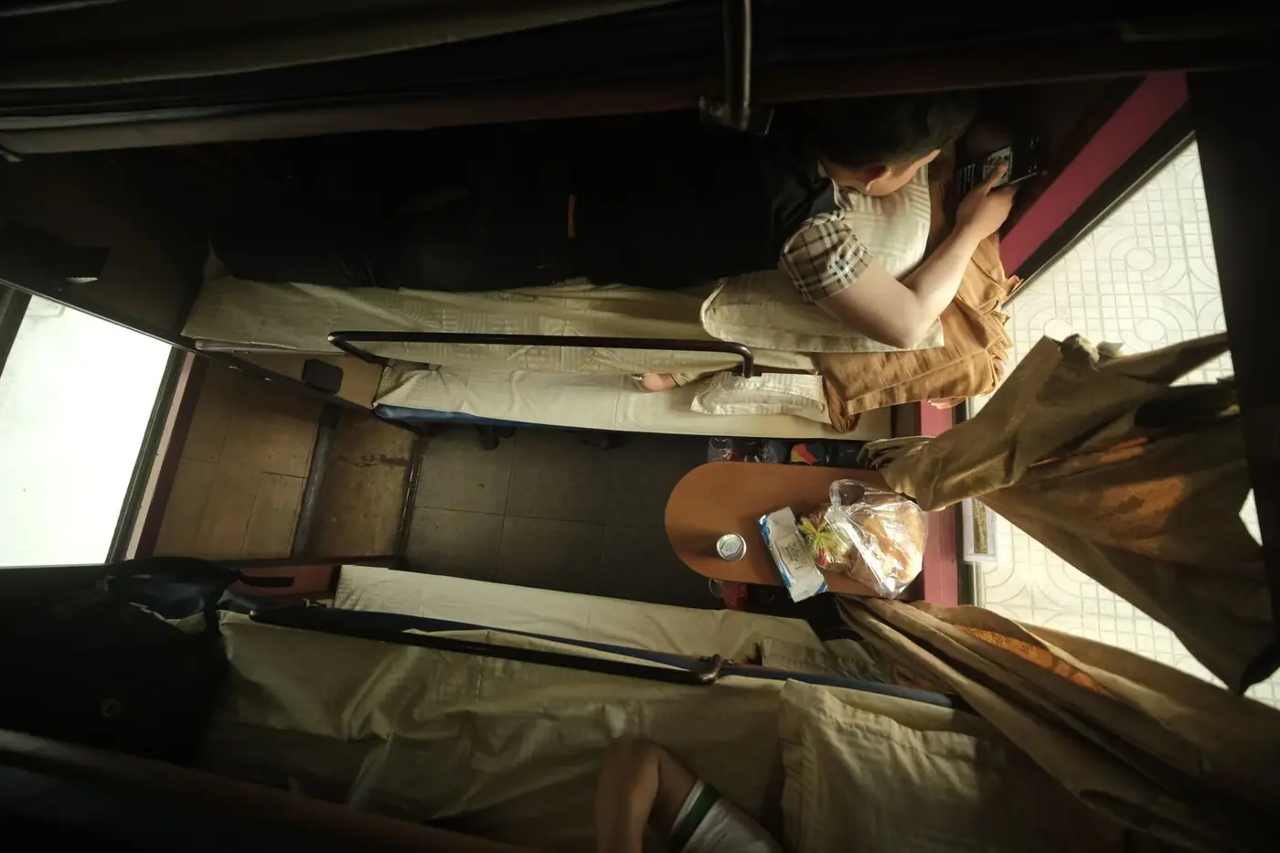 Overhead view of a two-tier sleeper berth with a passenger checking a phone