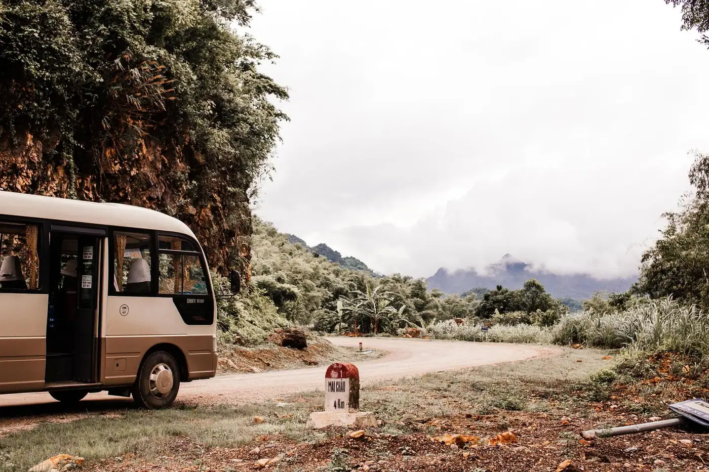 Small tour bus parked on a mountain road in northern Vietnam with a Mai Chau distance marker