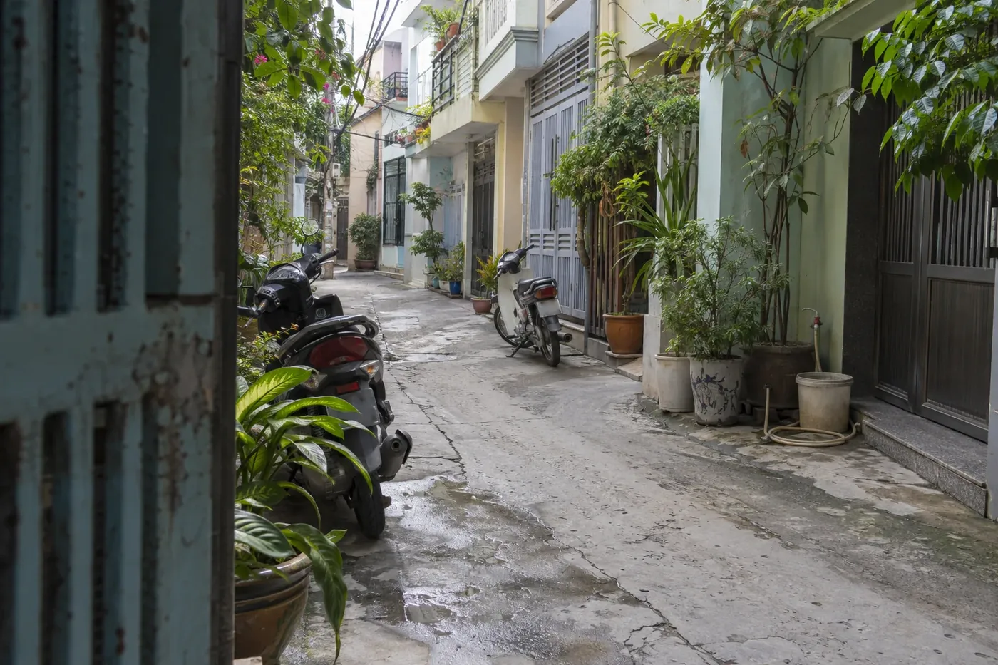Narrow wet alley with scooters parked at the entrance of a house