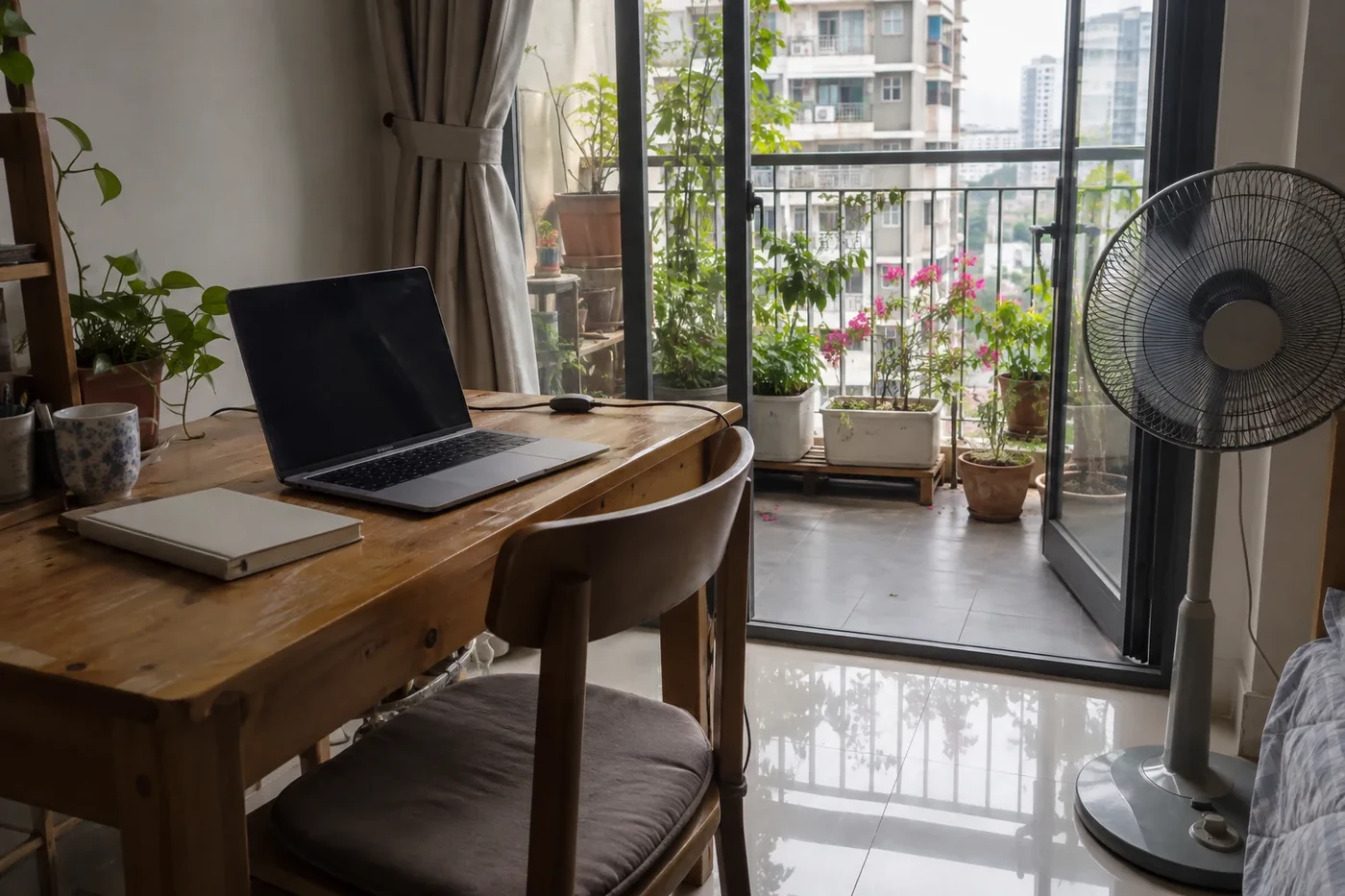 Laptop on a desk next to a fan and a balcony door
