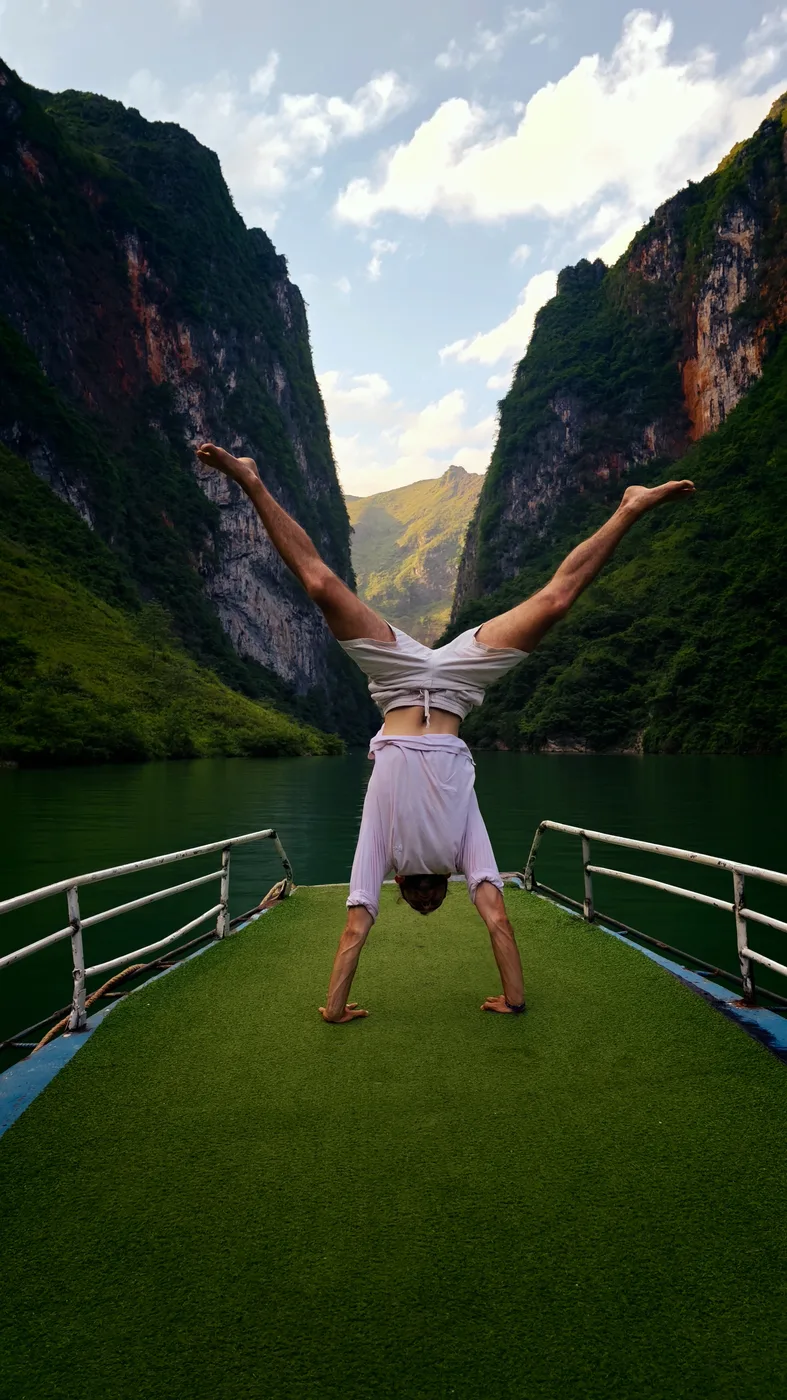 A traveler handstands on a boat gliding through Nho Que canyon