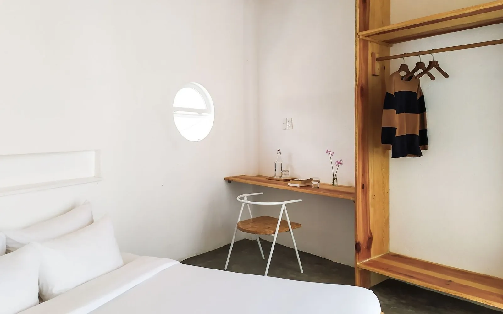 Minimalist guesthouse bedroom with a single bed, small desk, and round window