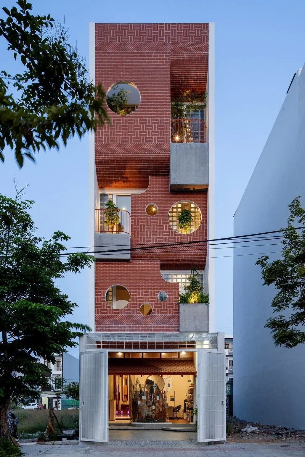 Modern red-brick apartment building facade with plant-filled balconies at dusk