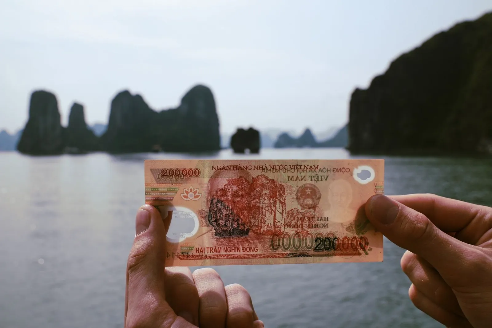 Hands holding a 200,000 Vietnamese dong banknote with Ha Long Bay in the background