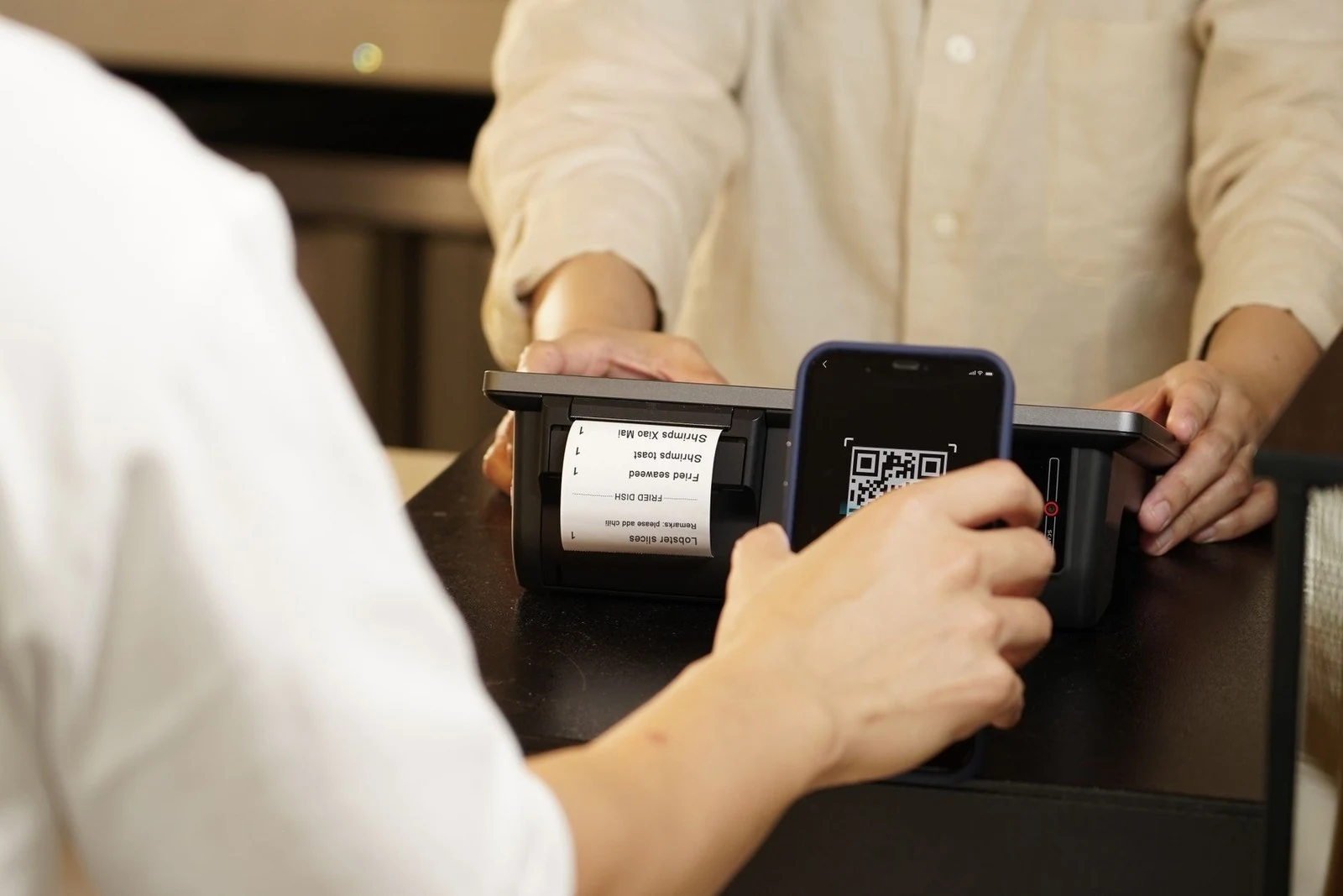 A customer scanning a QR code with a phone to pay at a counter