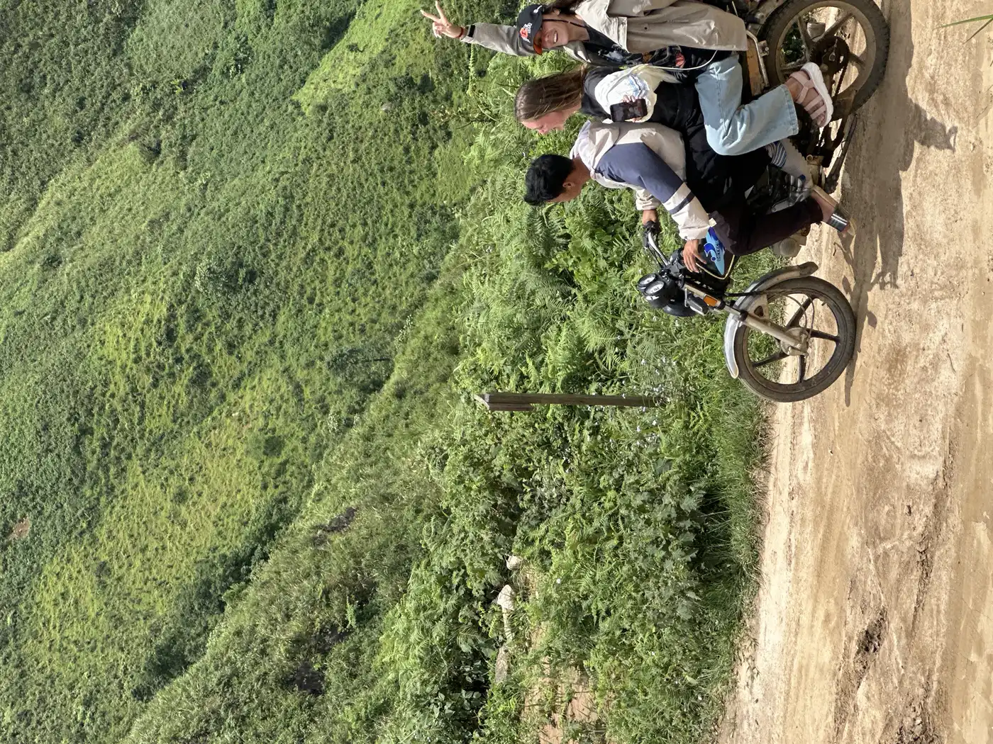 Three riders on a motorbike along a dirt mountain road