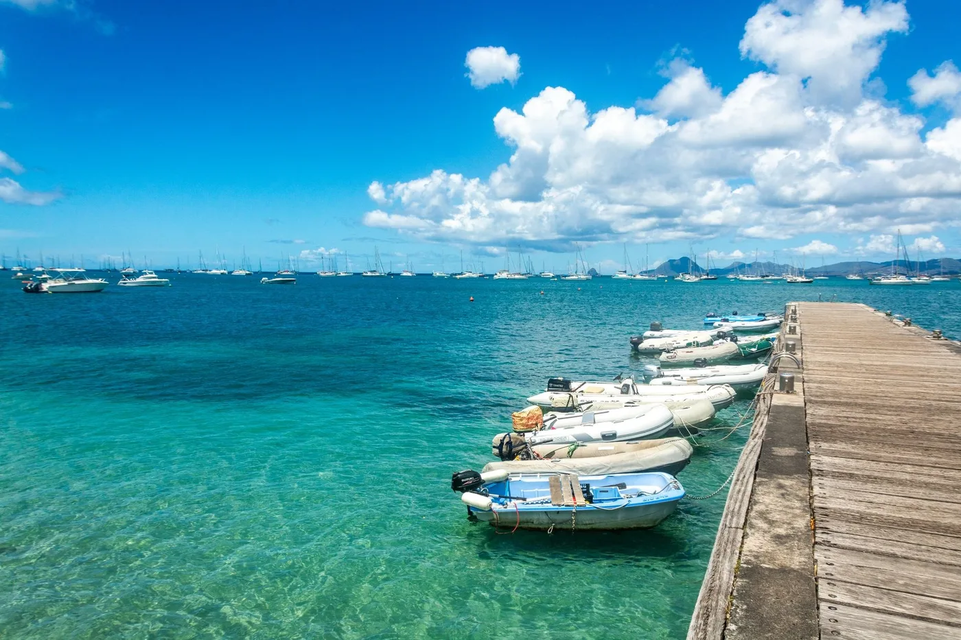 Small boats moored along a wooden pier with a marina in the background
