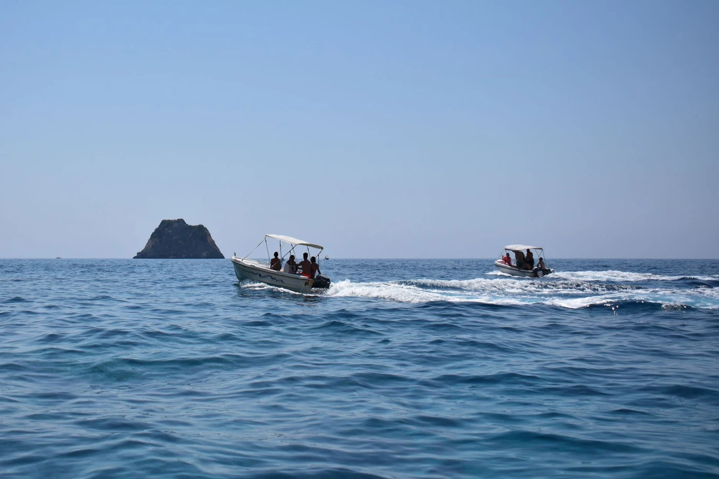 A speedboat cutting across calm blue water leaving a white wake