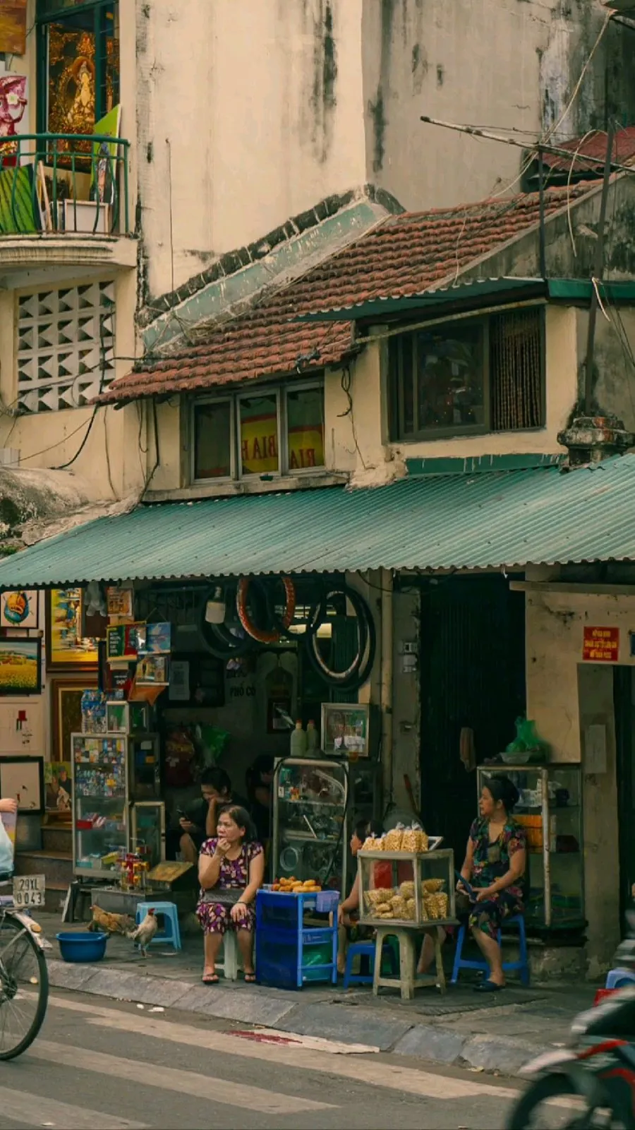 Street vendors sitting outside a shopfront with a green awning in old-quarter Vietnam