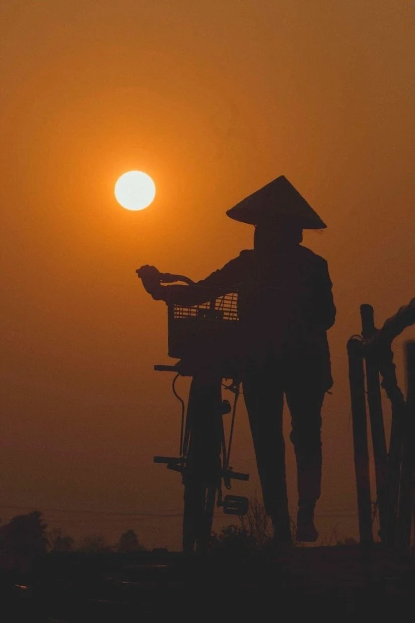 Traveler with a bicycle silhouetted at sunset on a Vietnam road