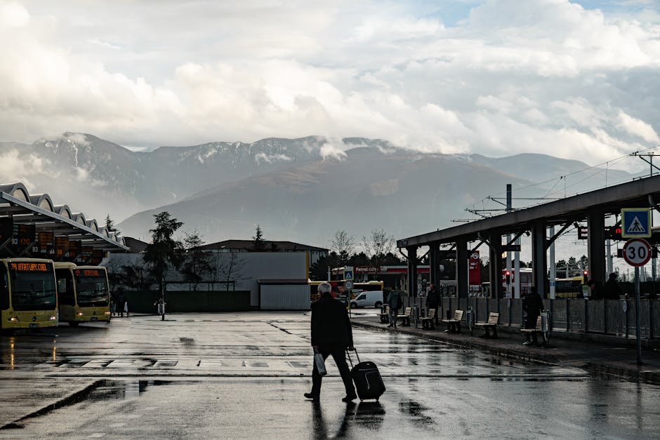 Bus terminal with a traveller wheeling luggage and cloudy mountain backdrop