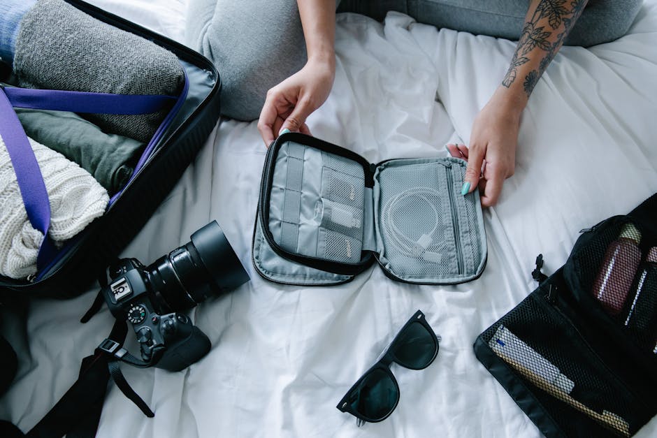 Travel essentials laid out on a hotel bed: camera, packing cubes, sunglasses, organiser