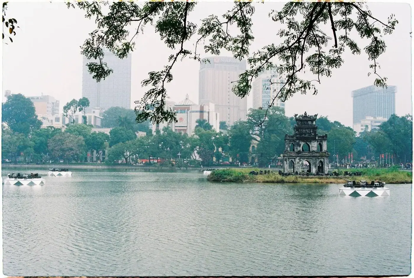 Hoan Kiem Lake and Turtle Tower framed by tree branches with Hanoi skyline behind