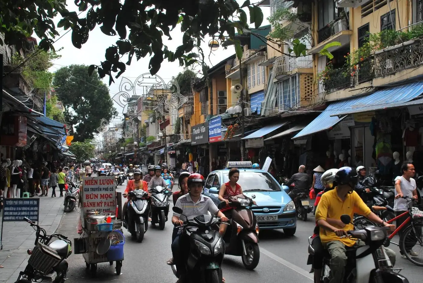 Dense motorbike and car traffic on a narrow shopping street in Hanoi