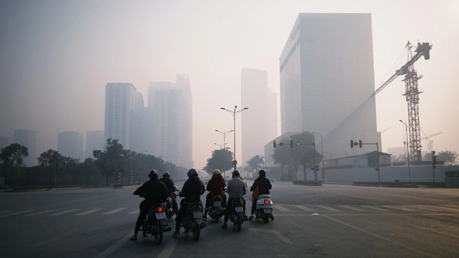 Motorbike riders in heavy smog facing a row of high-rise buildings