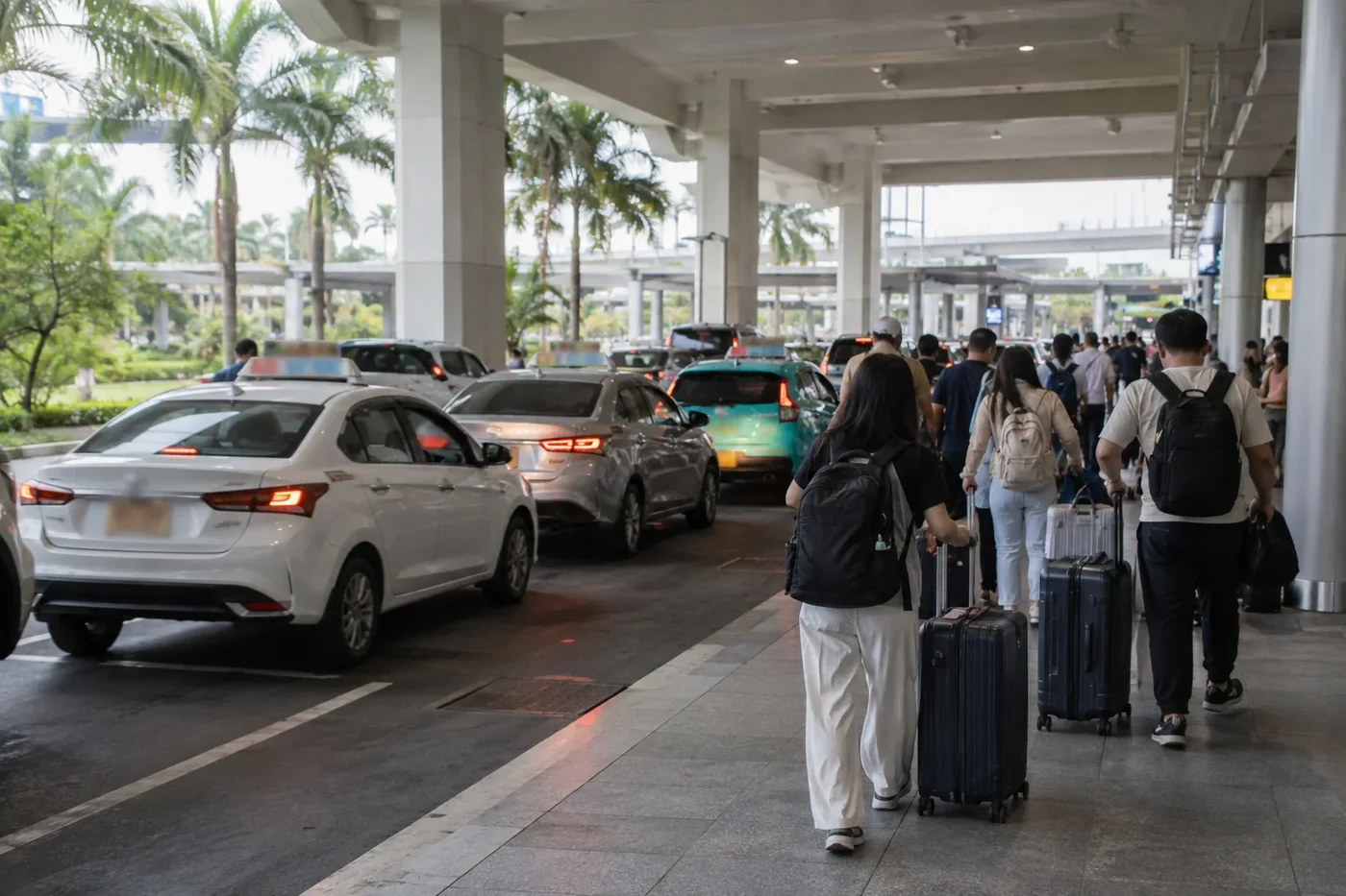 Travelers with suitcases walking past taxis at an airport arrivals curb