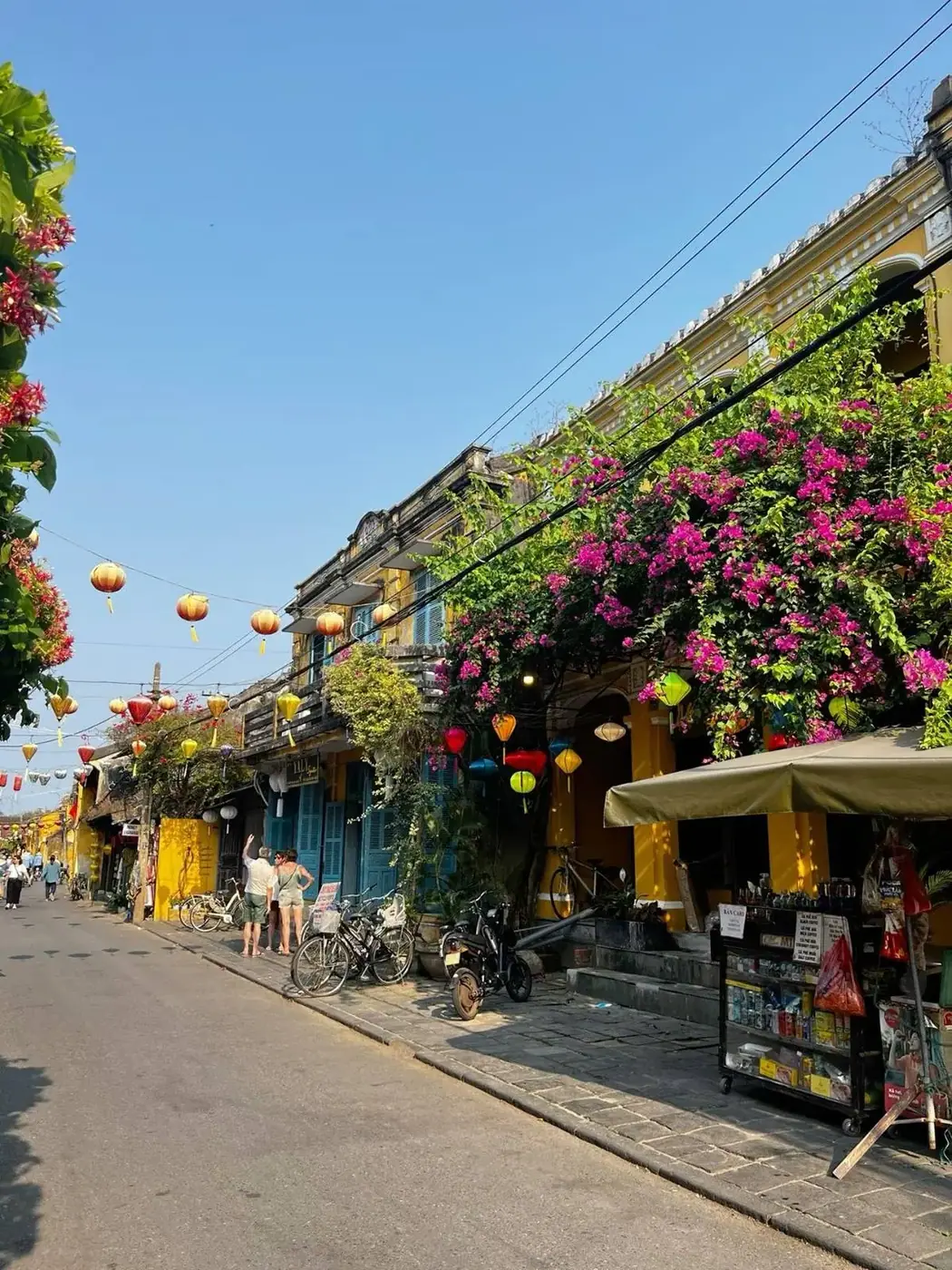 A sunny street in Hoi An with bicycles, motorbikes and a small shop
