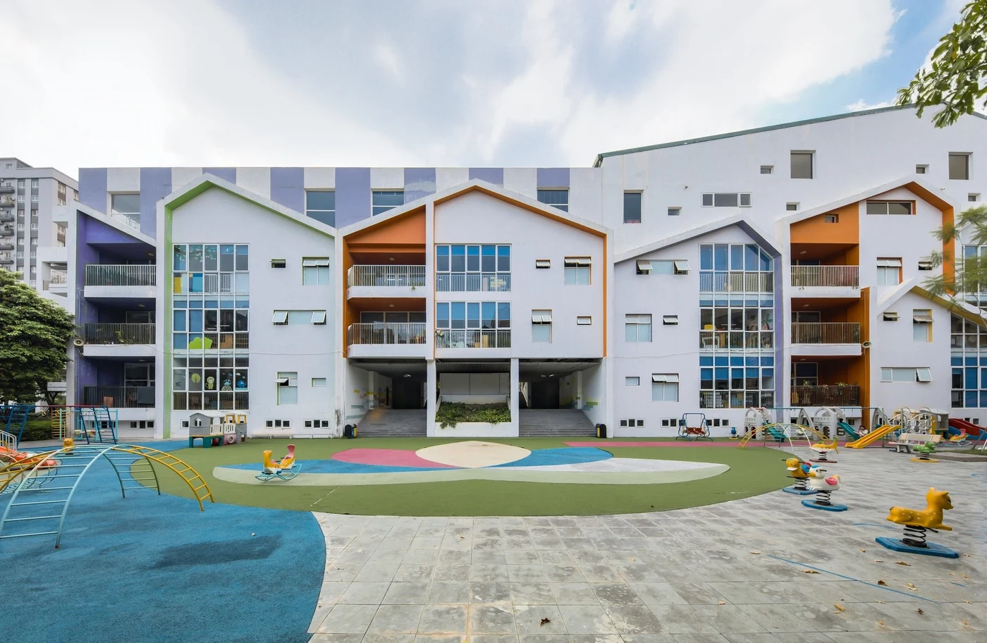 White school building with coloured gables above a play yard with ride-on toys and climbing frames