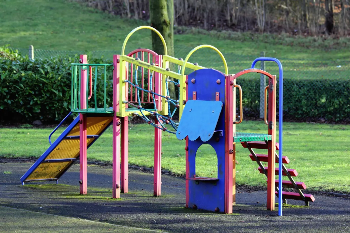 Colourful metal climbing frame with a ladder, net bridge and slide on a rubber playground surface