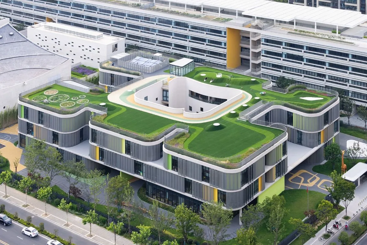 Aerial view of a school building with a green rooftop play area and curved facade