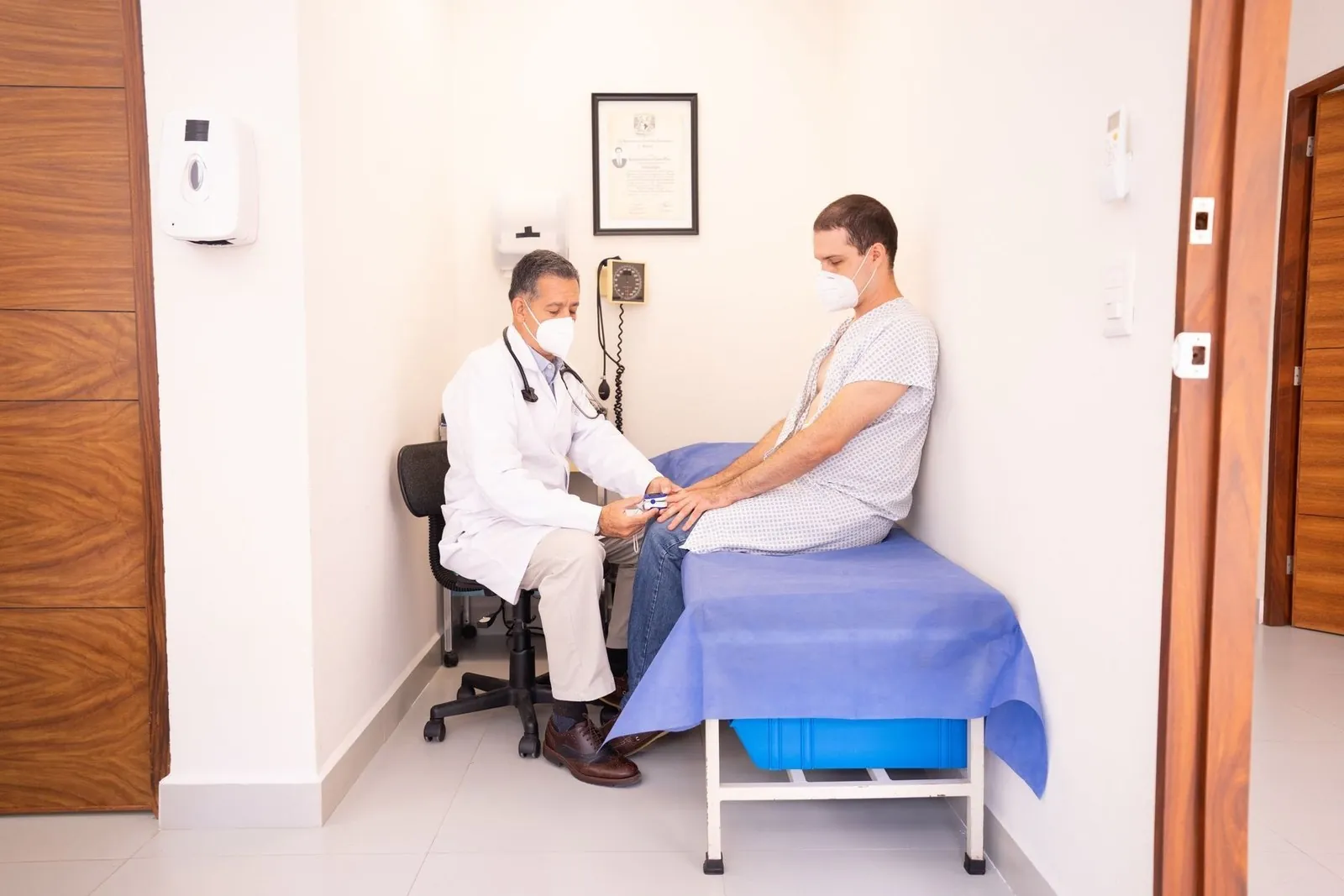 Doctor examining a masked patient in an exam room