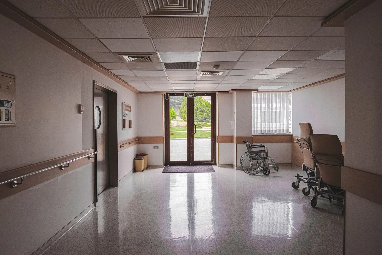Empty hospital corridor with wheelchairs near an exit door