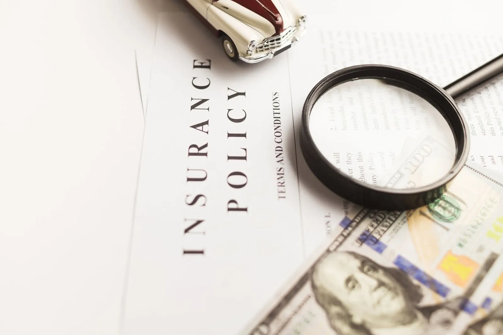 Insurance policy document under a magnifying glass with cash