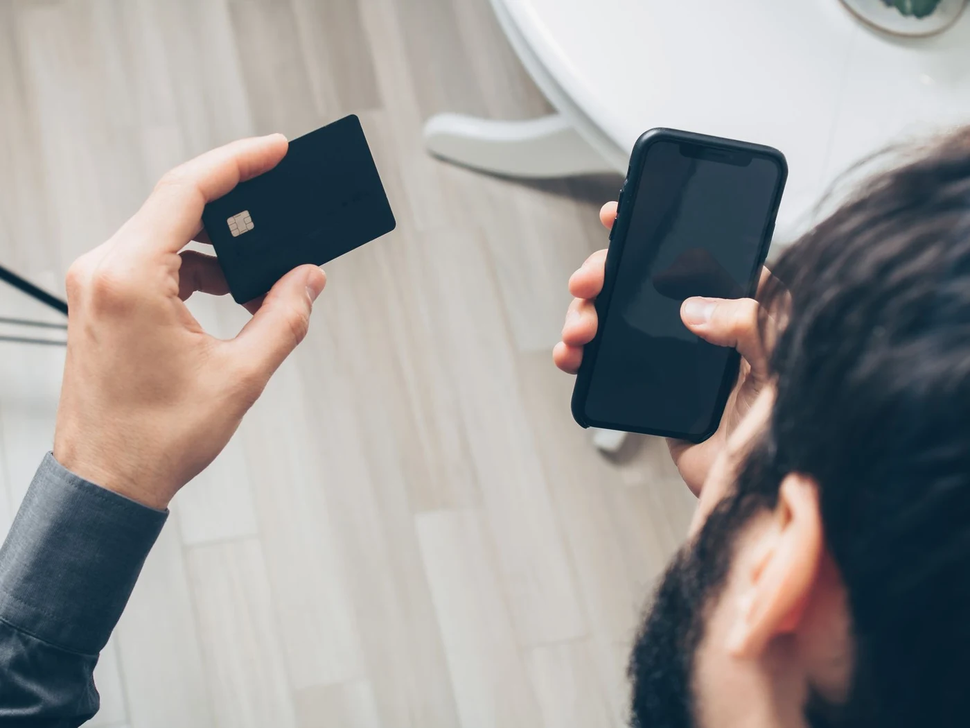 A man holding a black bank card in one hand and a smartphone in the other