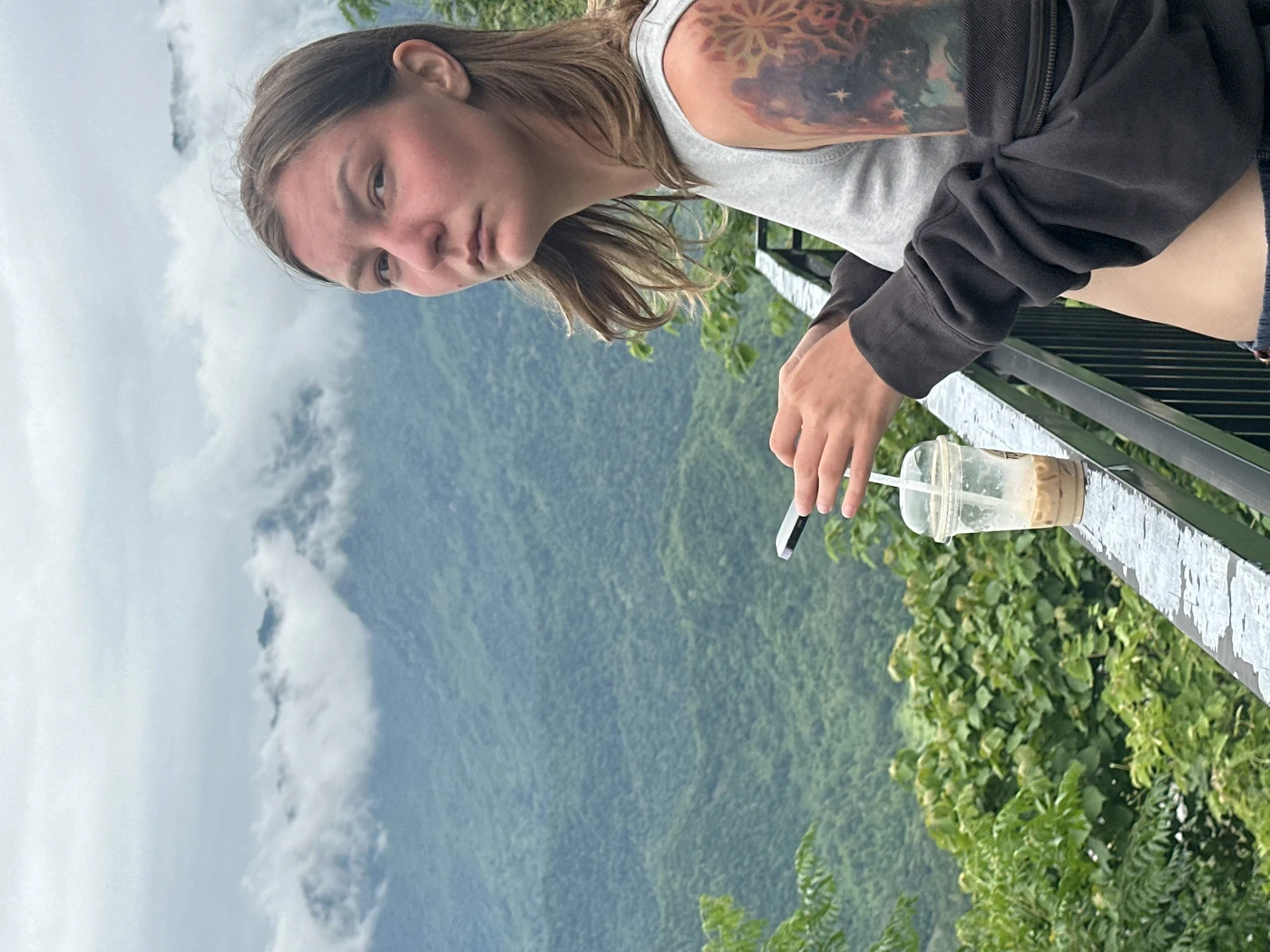 Woman with an iced coffee overlooking cloud-covered mountains in Sapa