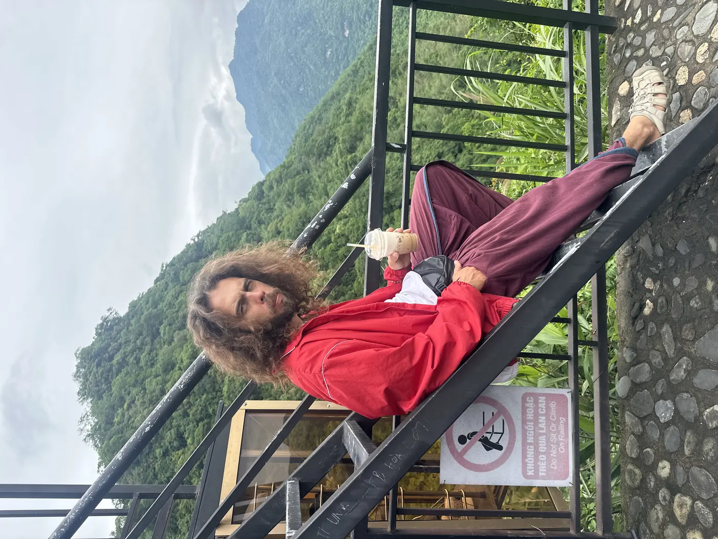Traveler resting on a stairway railing above misty green mountains in Sapa