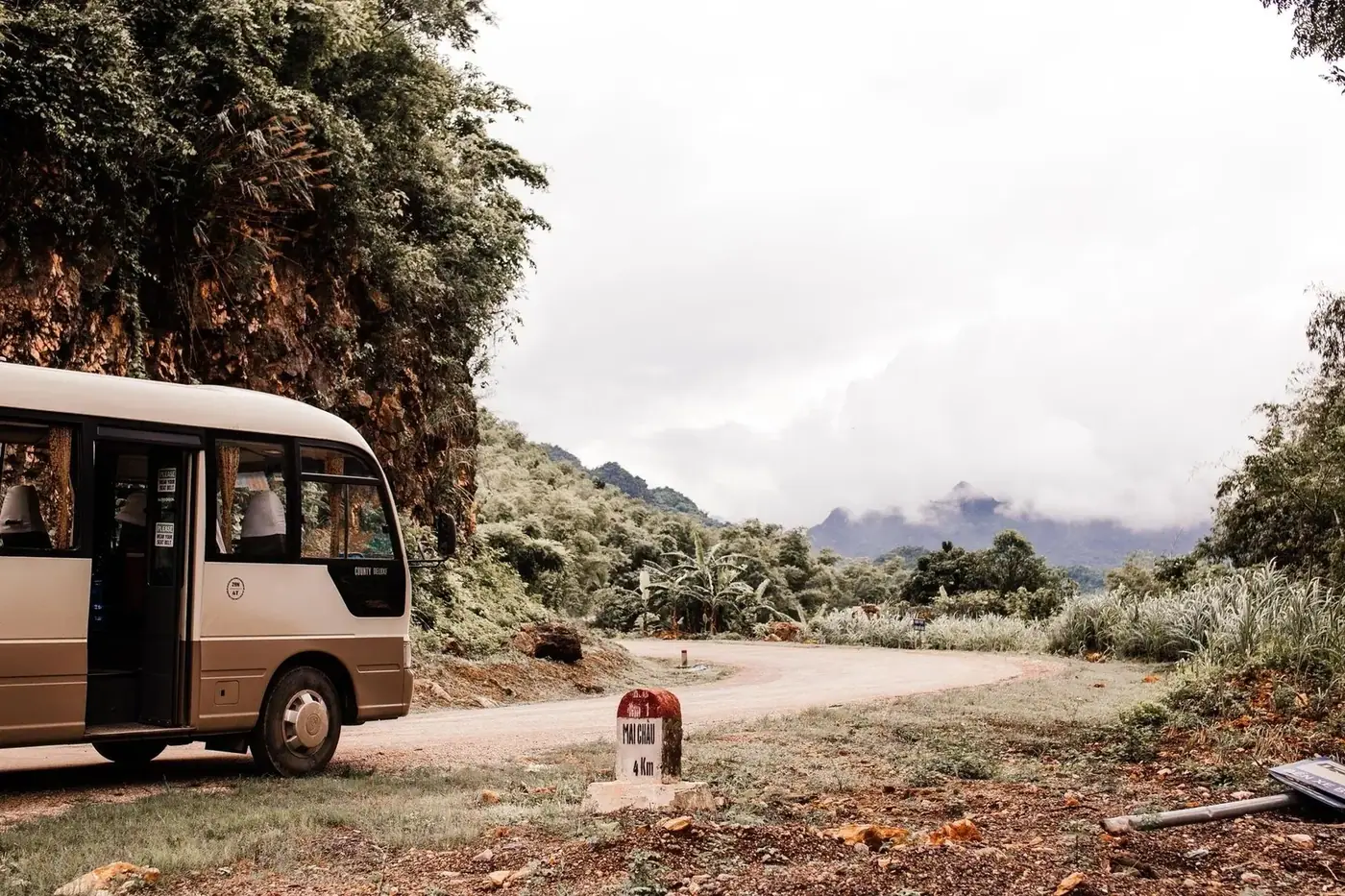 A minibus parked on a mountain road beside a highland route marker in Vietnam