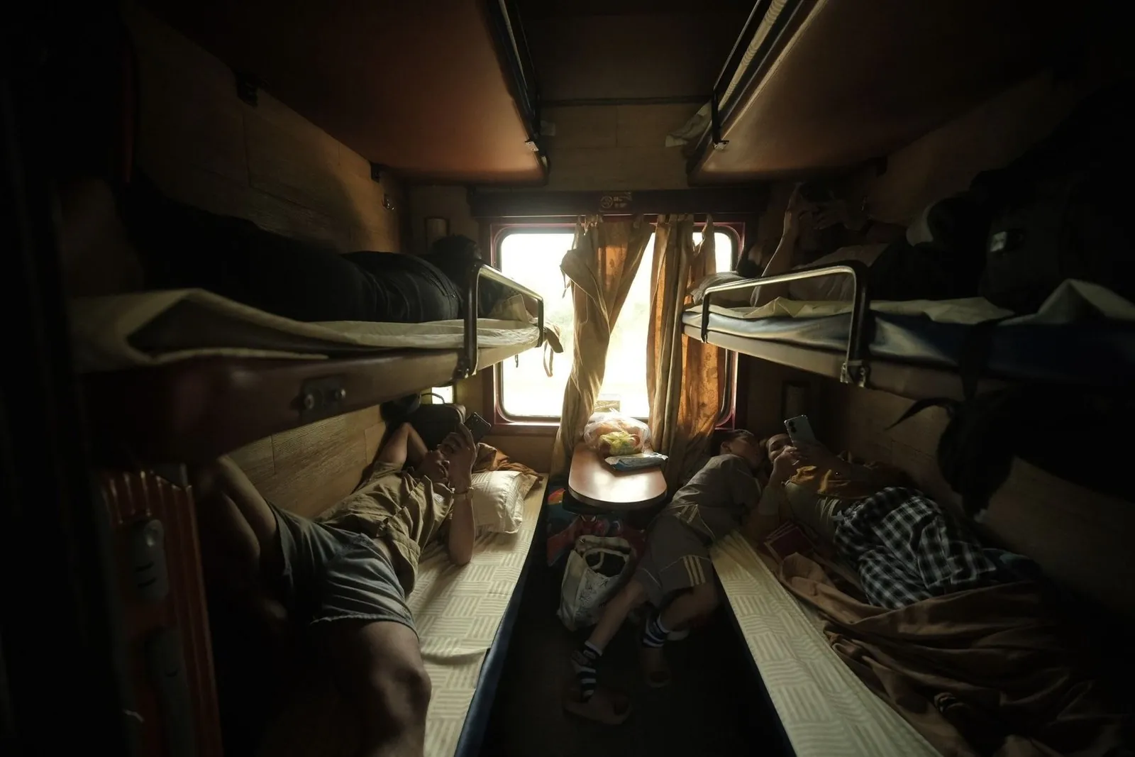 Passengers resting in a bunk-bed sleeper cabin with curtains