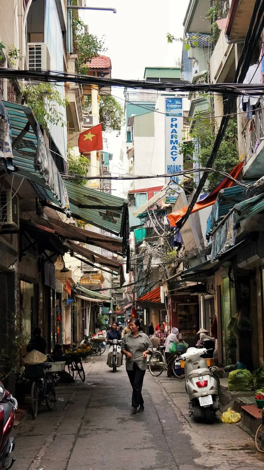 A narrow shopping street in Vietnam lined with shopfronts and scooters