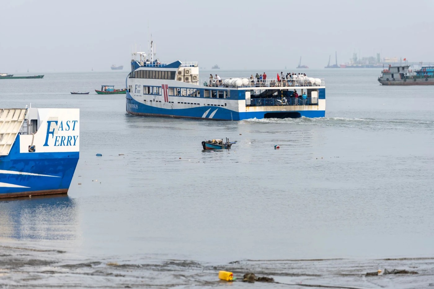 Passenger fast ferry moving through a harbor beside another boat with Fast Ferry lettering