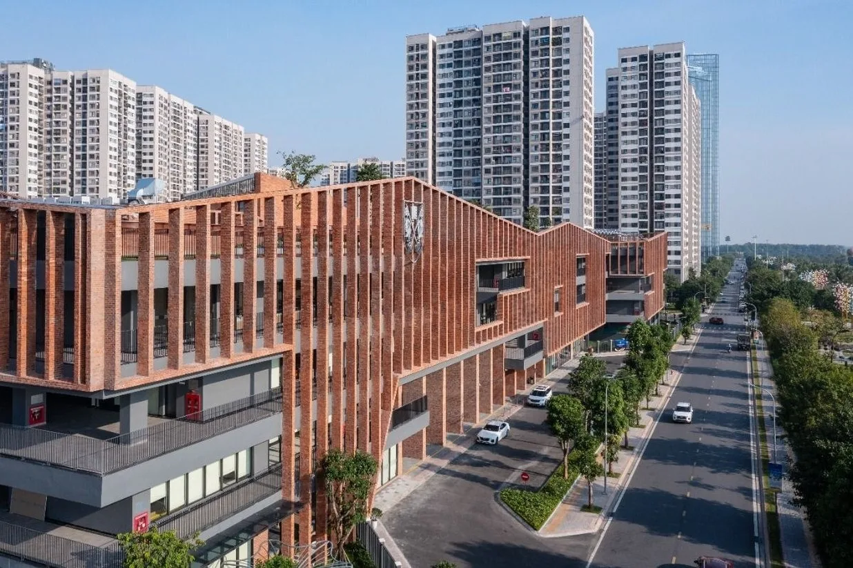 Large red brick school campus beside a tree-lined road