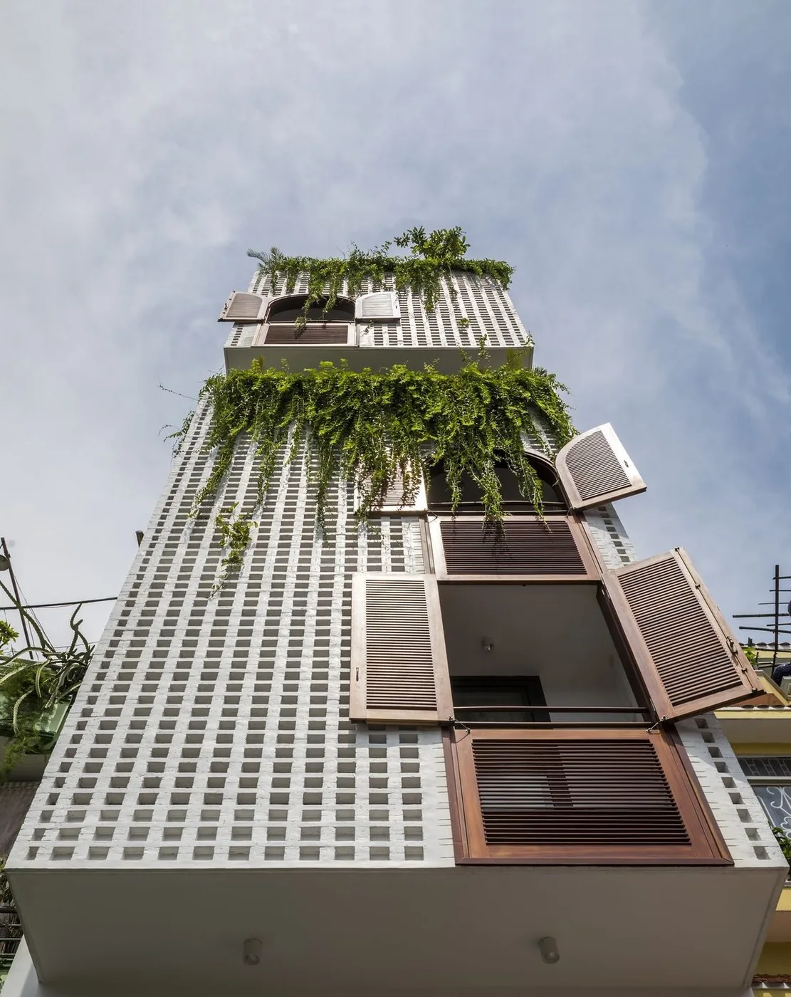 tall apartment tower with a perforated concrete facade and hanging plants