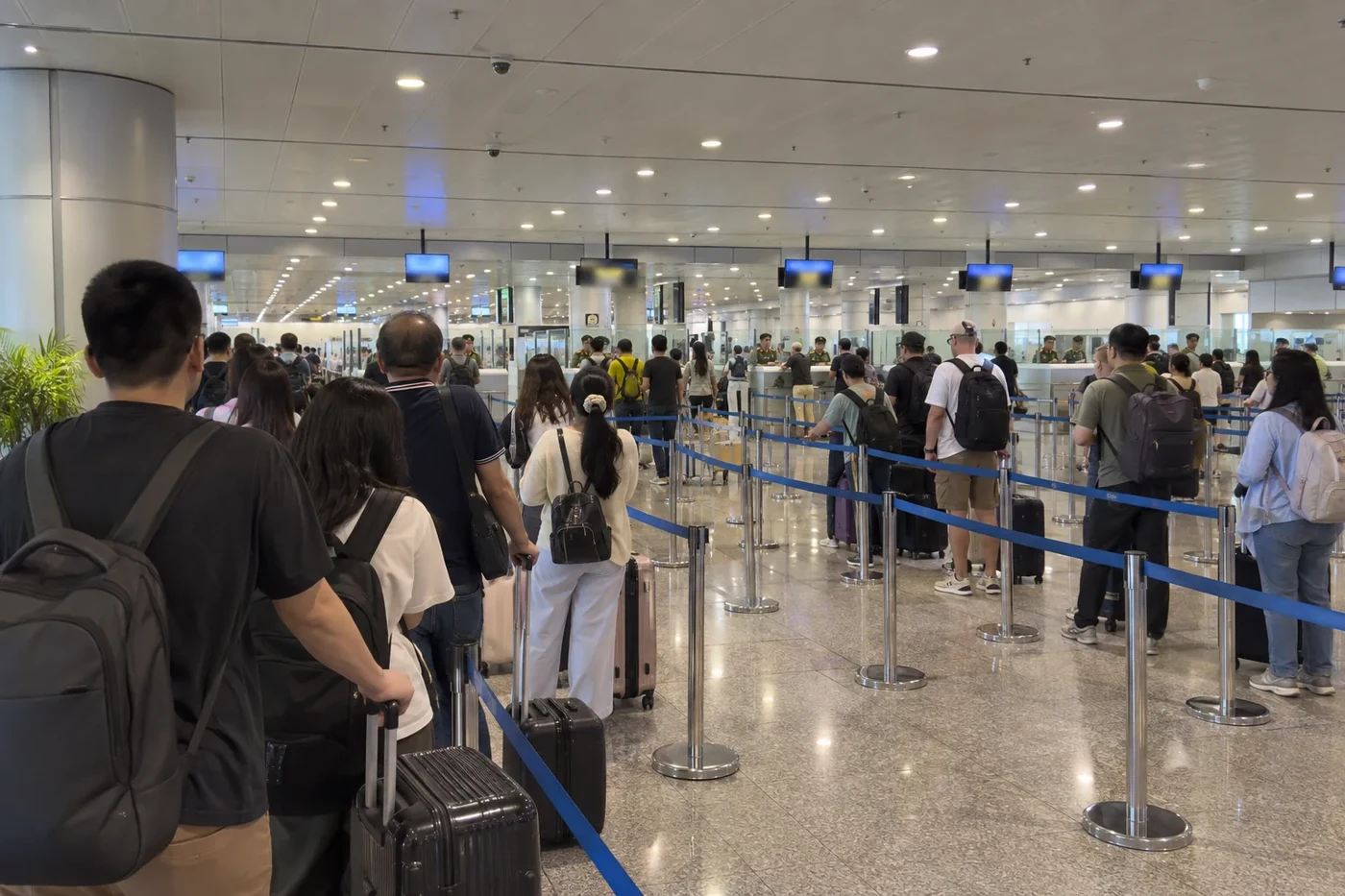 Passengers queuing at an airport passport control hall behind blue barriers