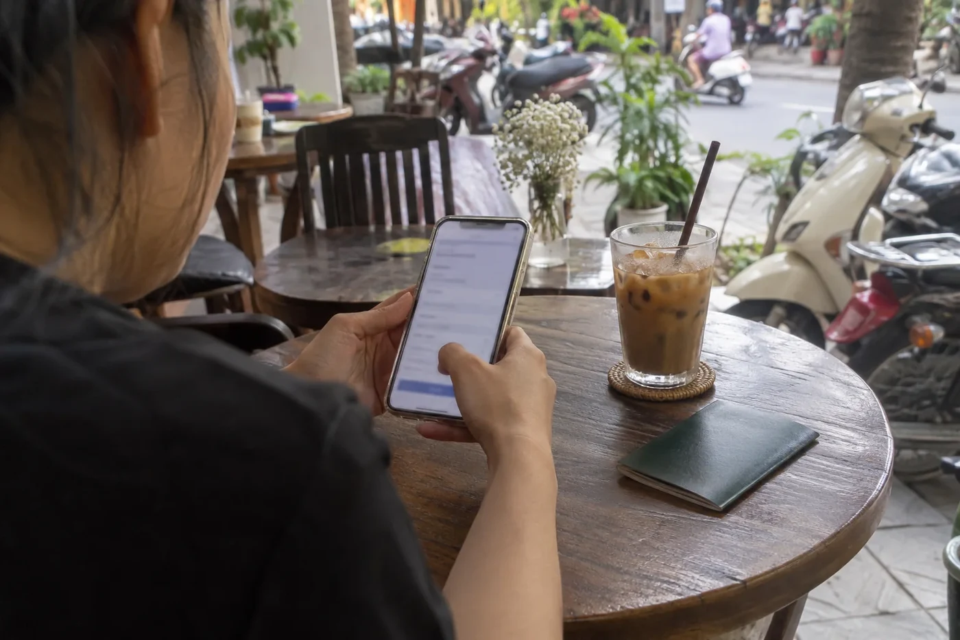 Hand holding a phone with an online form beside a passport on a cafe table