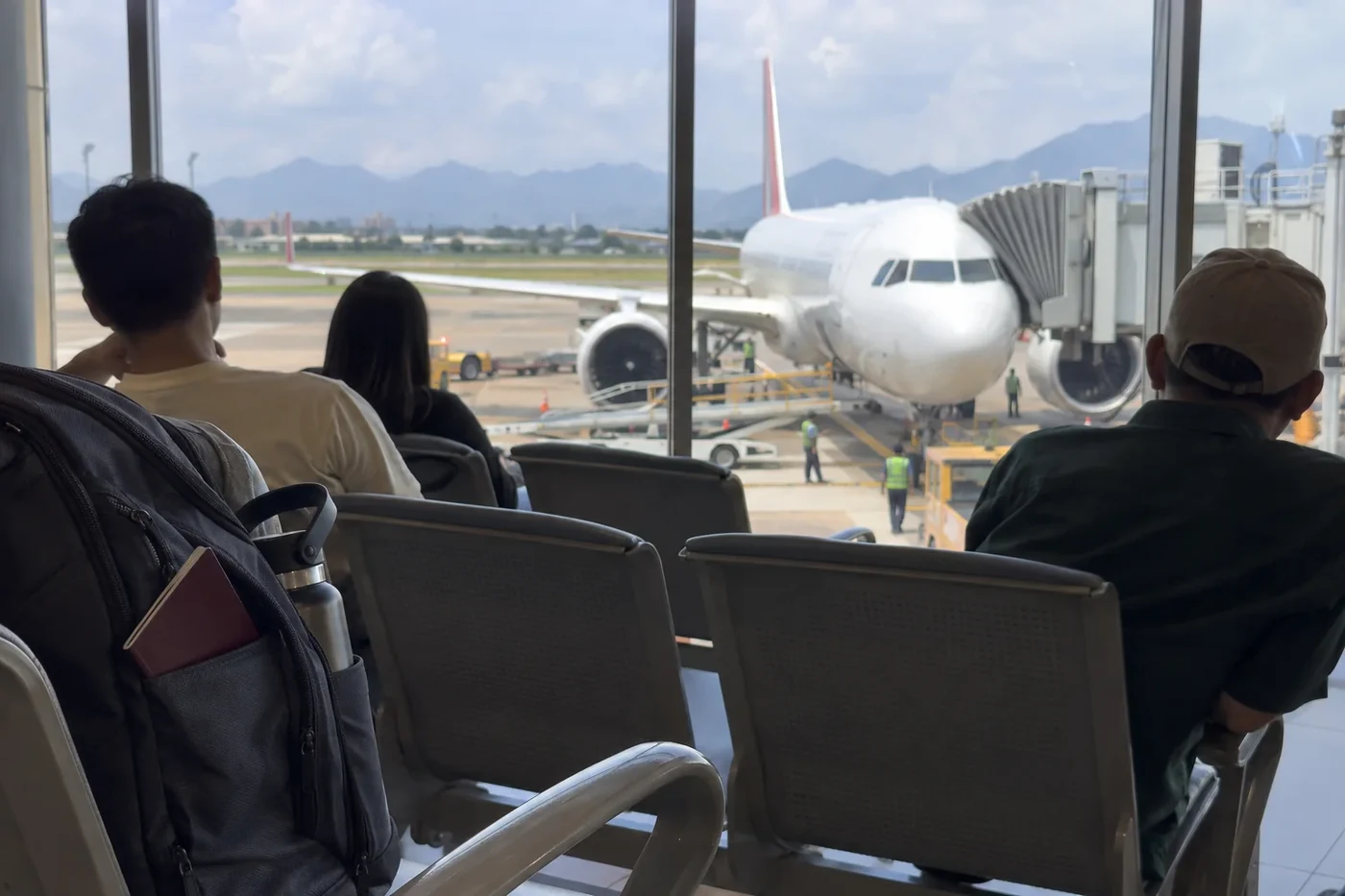 Travelers waiting at a boarding gate window with a plane on the apron