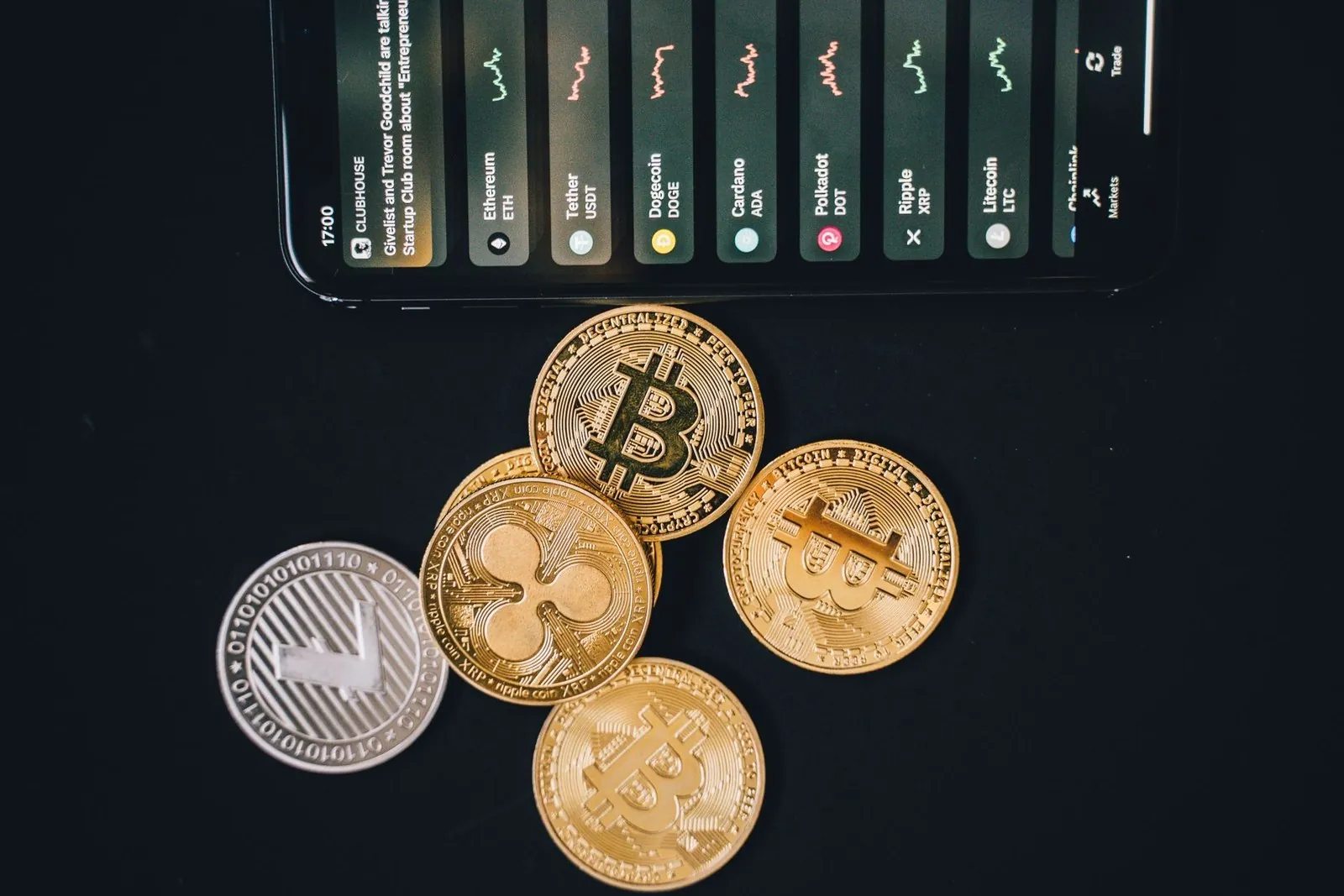 Gold and silver cryptocurrency coins next to a phone showing a trading app