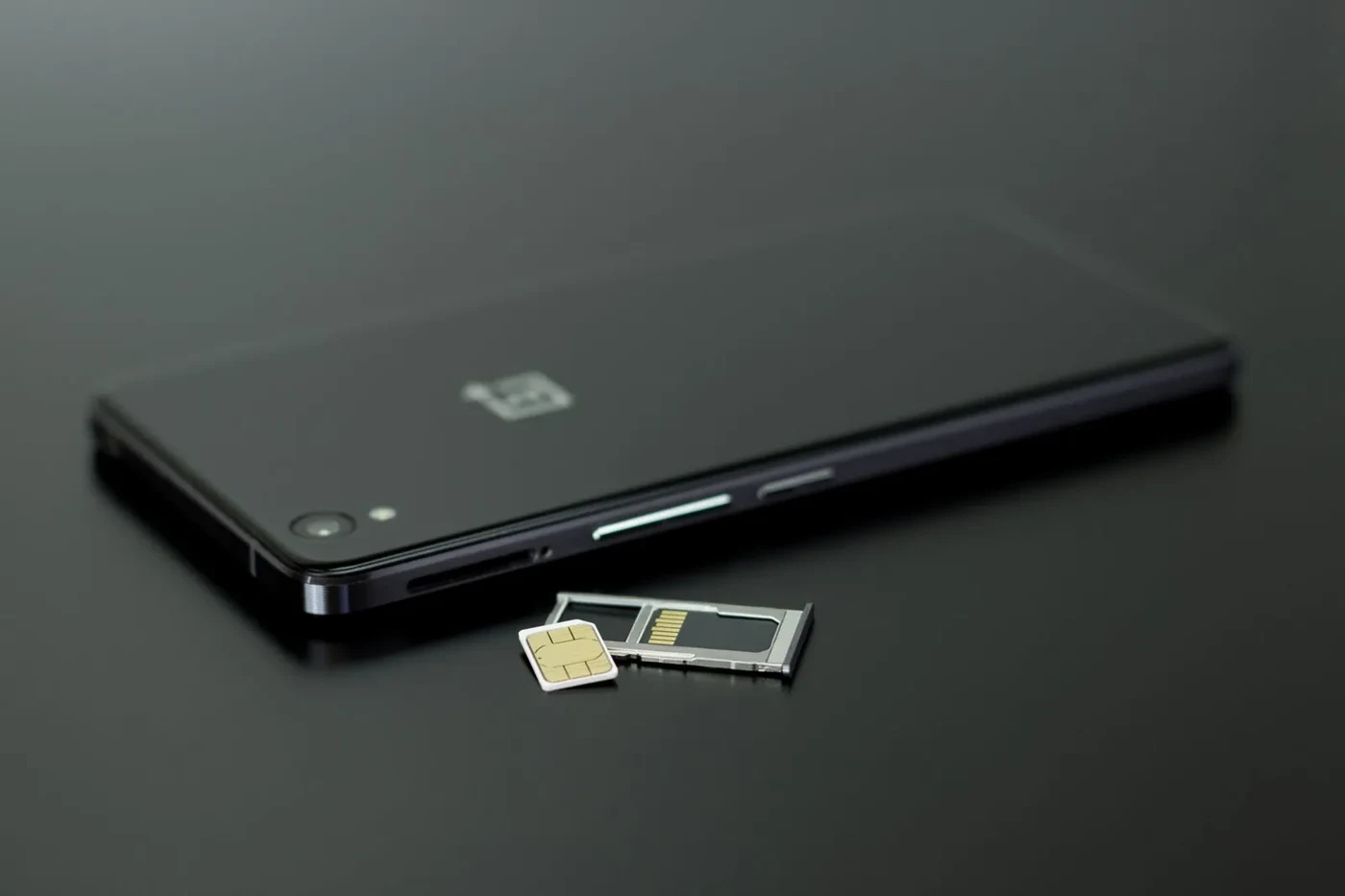 Black smartphone lying next to its open SIM tray with a nano SIM card