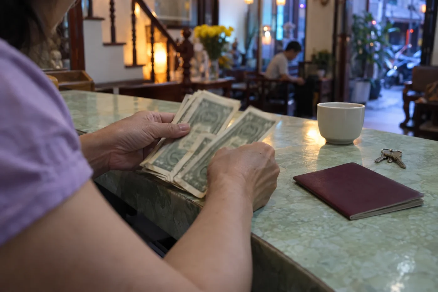 Hands counting dollar bills at a counter beside a passport and keys