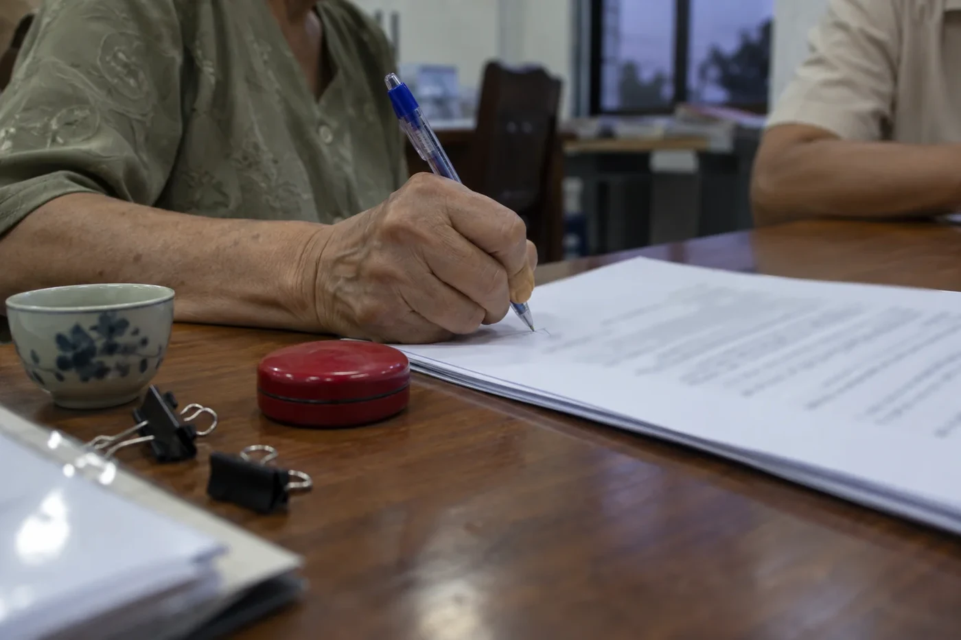 A hand signing a printed document next to a red stamp pad